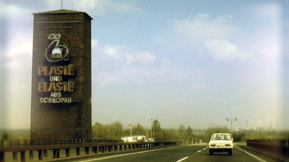 Turm neben Straße mit Werbung für die Buna-Werke Schkopau - Plaste und Elaste aus Schkopau.