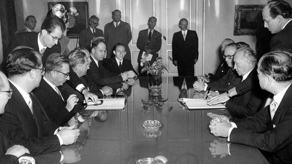 Der israelische Außenminister Moshe Sharett und der deutsche Bundeskanzler Konrad Adenauer unterzeichnen einen Vertrag.