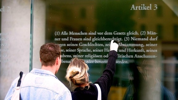 Junges Paar liest das Grundgesetz auf einer Glasfläche am Jakob-Kaiser-Haus im Berliner Regierungsviertel