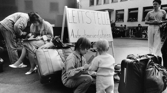 Historisches Schwarzweiß-Foto: Angekommene Übersiedler aus der DDR füllen ihre Aufnahmeformalitäten aus. Daneben ein Schild: Leitstelle Aufnahmeverfahren.