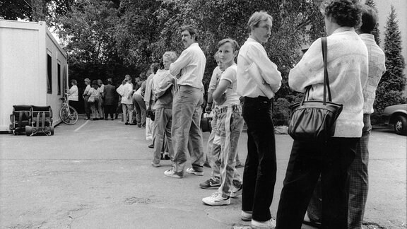 Historische Schwarzweiß-Aufnahme: Menschen stehen vor einem Container in einer Reihe.