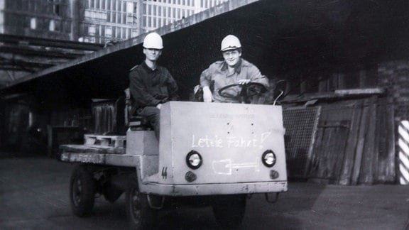 Zwei Bausoldaten sitzen auf einem kleinen offenen Transporter.