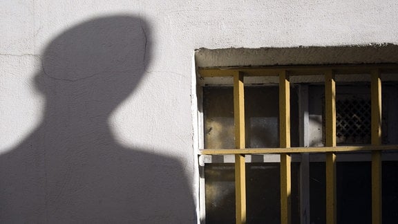 Der Schatten eines Mannes ist neben dem letzten erhaltenen Gitterfenster des ehemaligen Geschlossenen Jugendwerkhofes Torgau in der heutigen Gedenkstätte in Torgau zu sehen