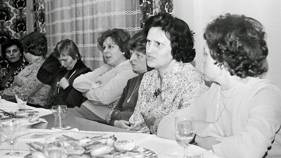Sechs Frauen sitzen an einer Kaffeetafel und diskutieren. 