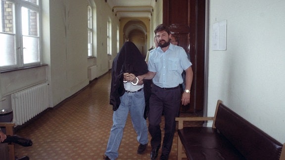 In Handschellen und unter der Robe seines Anwaltes verborgen, verläßt am 18.07.1994 einer der Angeklagten im Magdeburger Prozeß gegen mutmaßliche Haupttäter der sogenannten Himmelfahrtskrawalle den Gerichtssaal. 