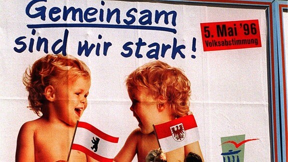 Zwei Passanten stehen vor einem Werbeplakat zur Volksabstimmung über die Länderfusion von Berlin und Brandenburg im Mai 1996 (Archivfoto vom 29.04.1996).