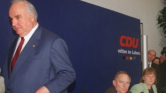 Alt-Bundeskanzler Helmut Kohl (l), der am 30.11.1999 in Berlin frühzeitig eine Pressekonferenz zur CDU-Spendenaffäre verlässt, die er zusammen mit dem damaligen CDU-Vorsitzenden Wolfgang Schäuble (M) und Angela Merkel (r), damals Generalsekretärin der Partei, gegeben hatte.