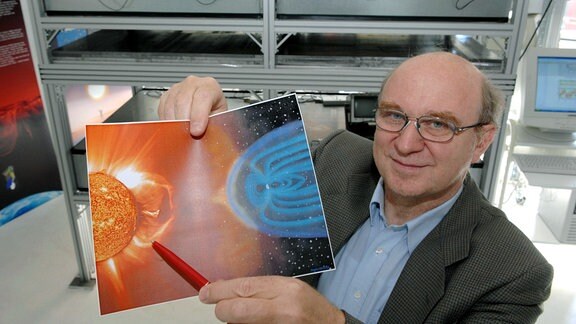 Der Projektleiter der Universität Greifswald für das Weltraumwetter-Myonen-Teleskop (im Hintergrund), Physik-Professor Rainer Hippler, zeigt am Donnerstag (31.05.2007) in Greifswald auf einer Abbildung einen Bereich der Sonnenoberfläche, wo Sonnenwinde entstehen.