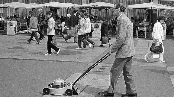 Ein Mann geht mit einem Rasenmäher auf der Straße.