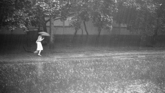 Eine Frau rennt mit Regenschirm durch den Regen.