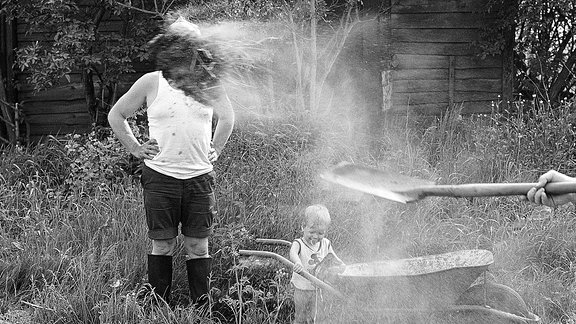 Ein Mann und ein Kind werden mit einem Wasserschlauch nass gemacht.