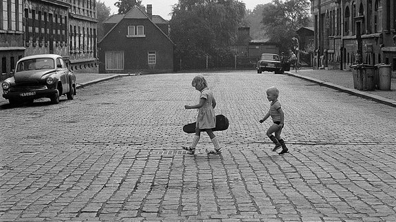 Zwei Kinder laufen über einer gepflasterte Straße.