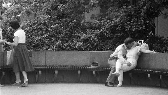 Ein Pärchen küsst sich auf einer Parkbank.