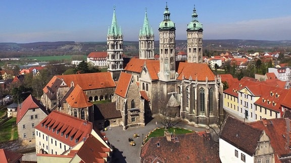 Blich über die Dächer auf den Naumburger Dom: kreuzförmiges Gebäude mit vier Türmen und roten Dächern.