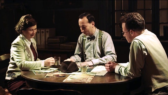 Eine Frau und zwei Männer sitzen an einem Tisch