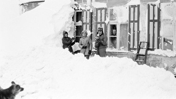 Drei Menschen stehen vor einem zugeschneiten Haus.