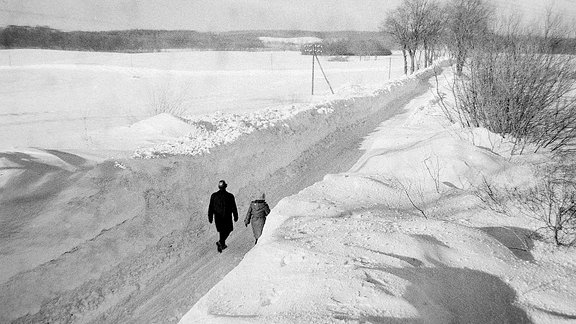 Zwei Menschen laufen zwischen hohen Schneewänden eine Straße entlang.