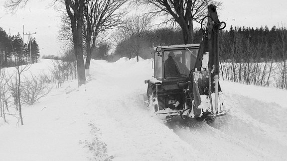 Ein Bagger fährt über eine mit Schnee bedeckte Straße.