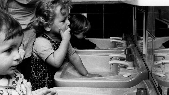 Kinder waschen sich unter Anleitung der Erzieherin in einem Kindergarten an einem Waschbecken die Hände