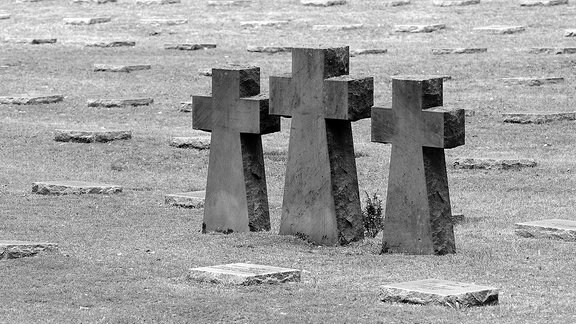Drei Steinkreuze und Grabplatten auf einem Soldatenfriedhof