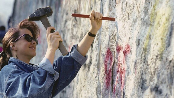Junges Mädchen bearbeitet mit Hammer und Meißel die Berliner Mauer 