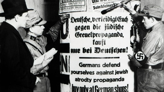 Mitglieder der SA (Sturmabteilung) kleben Plakate auf eine Litfaßsäule mit den Worten: Deutsche, verteidigt Euch gegen die jüdische Greuelpropaganda, kauft nur bei Deutschen!, 1933.