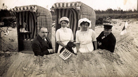 Vier Strandbesucher hinter Sandhügel vor Strandkörbe, um 1935