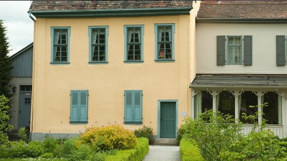 Schillerhaus in Jena. Ehemaliges, renoviertes, dreistöckiges, Bauernhaus mit gelber Fassade und grünen Fensterrahmen.