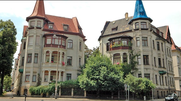 Dreistöckige Zwillingshäuser mit Türmchen, Balkons und Veranda aus der Gründerzeit an der Kreuzung Liviastraße/Feuerbachstraße/Tschaikowskistraße im Waldstraßenviertel in Leipzig, Aufnahme vom Juli 2014. Das linke Haus ist saniert, das Türmchen des rechten Hauses ist mit blauer Folie überspannt.