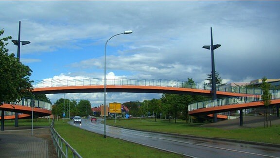 Brücke in Wernigerode. Orangefarbene Fußgängerbrücke mit großen Bögen als Zugang verbindet die beiden Plattenbauwohngebiete Burgbreite und Stadtfeld in Wernigerode, im Volksmund nach einem früheren Bürgermeister „Kilians Kreisel“ genannt.