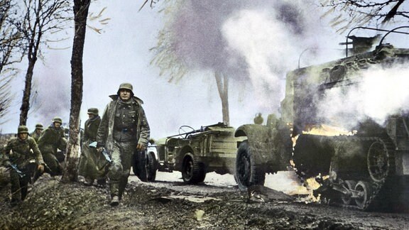 Deutsche Soldaten ziehen an brennender US-Ausrüstung vorbei.