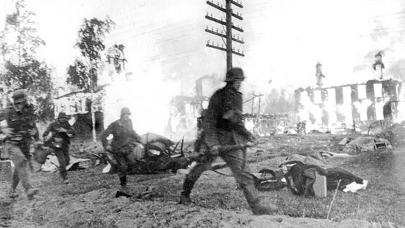 Deutsche Soldaten rennen durch einen brennenden Vorort Leningrads 1941.