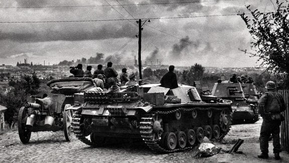 Deutsche Soldaten mit Panzerfahrzeugen beobachten Luftangriff auf Stadt in Frankreich 1940
