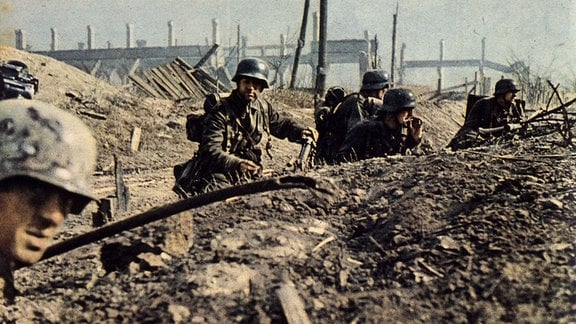 Wehrmacht-Soldaten kauern im Graben eines Schlachtfeldes.  