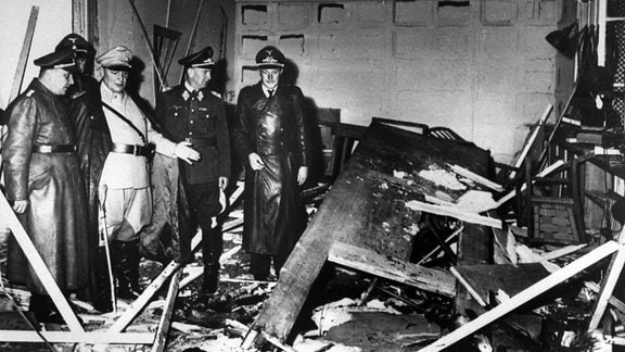 Mitglieder des deutschen Oberkommandos, darunter Hermann Göring (in Weiß) und Martin Bormann (links), begutachten die Schäden in einem Raum in Adolf Hitlers Hauptbunker „Wolfsschanze“.