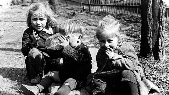 Ein schwarz-weiß Foto dreier Kinder die auf dem Boden hocken.