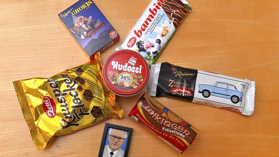 Verschiedene Süßigkeiten liegen auf einem Tisch neben einem Bild von Erich Honecker