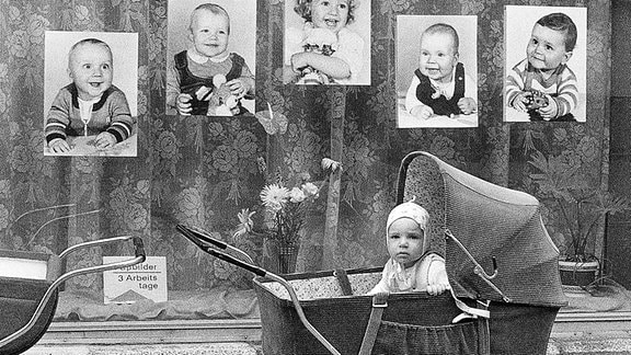Ein Kinderwagen mit Baby, steht vor einem Schaufenster in der DDR.