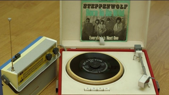 Kleiner Plattenspieler mit roter Verkleidung, darüber eine Schallplatte von Steppenwolf, daneben ein Transistorradio