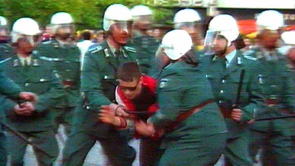 Volkspolizisten in grüner Monturr mit Helm halten Flüchtenden fest
