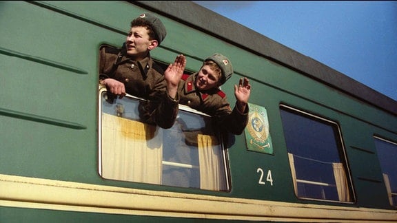 Zwei Soldaten winken aus dem abfahrenden Zug.