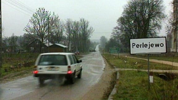 Rückansicht eines Autos neben Ortsdurchfahrtsschild mit Aufschrift "Perlejewo".
