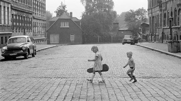 Zwei Kinder überqueren im Entenmarsch das Kopfsteinpflaster; Leipzig 1985
