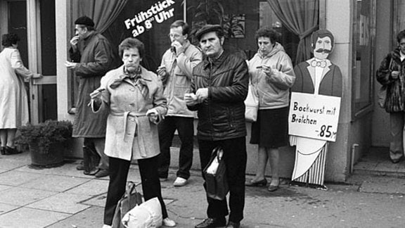 Männer und Frauen essen Bockwurst und kauen in den 80-er Jahren auf dem Leipziger Weihnachtsmarkt