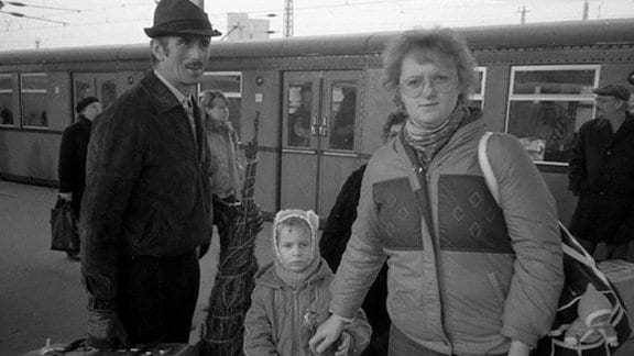 Familie mit eingewickelten Tannenbaum steht auf Bahnhof vor Zug in den 80-er Jahren in Leipzig.