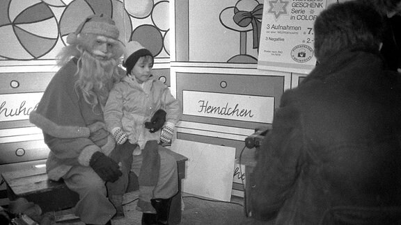 Kleiner Junge sitzt auf dem Schoß des Weihnachtsmann in den 80-er Jahren auf dem Leipziger Weihnachtsmann