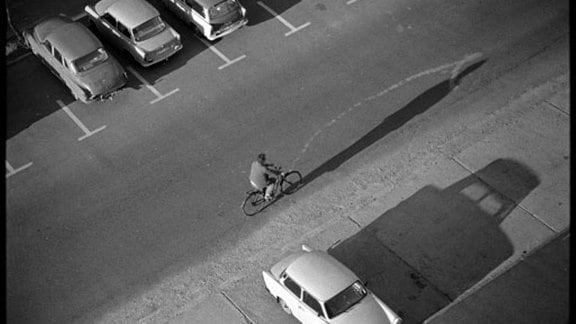 Parkende Autos, ein Radfahrer und lange Schatten.