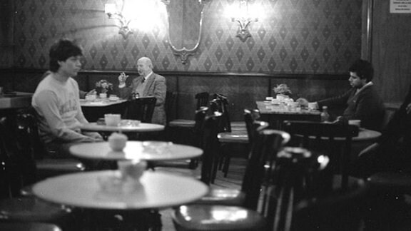 Männer sitzen an kleinen runden Tischen in einer Bar.