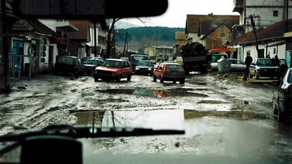 Blick aus einem Auto auf eine schlammige Straßen zwischen einer Häuserreihe