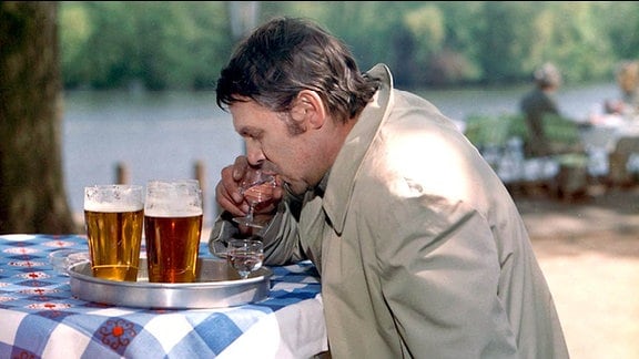 Ein Mann an einem Tisch mit karierter Decke, vor ihm stehen mehrere volle Gläser mit Bier 